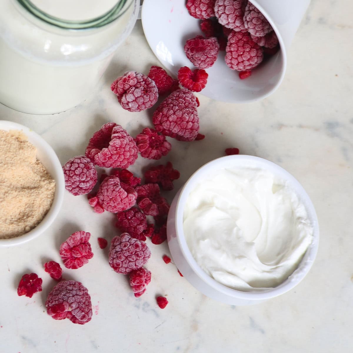 Raspberries, cream and other ingredients on a marble counter
