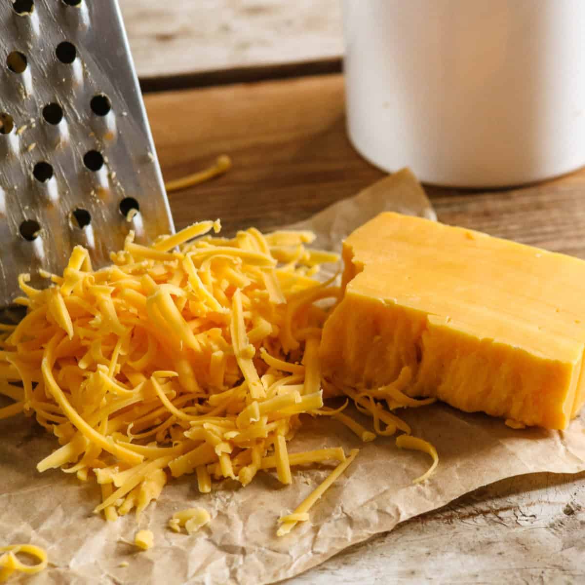 Grated cheddar cheese and a block of cheddar cheese next to a cheese grater