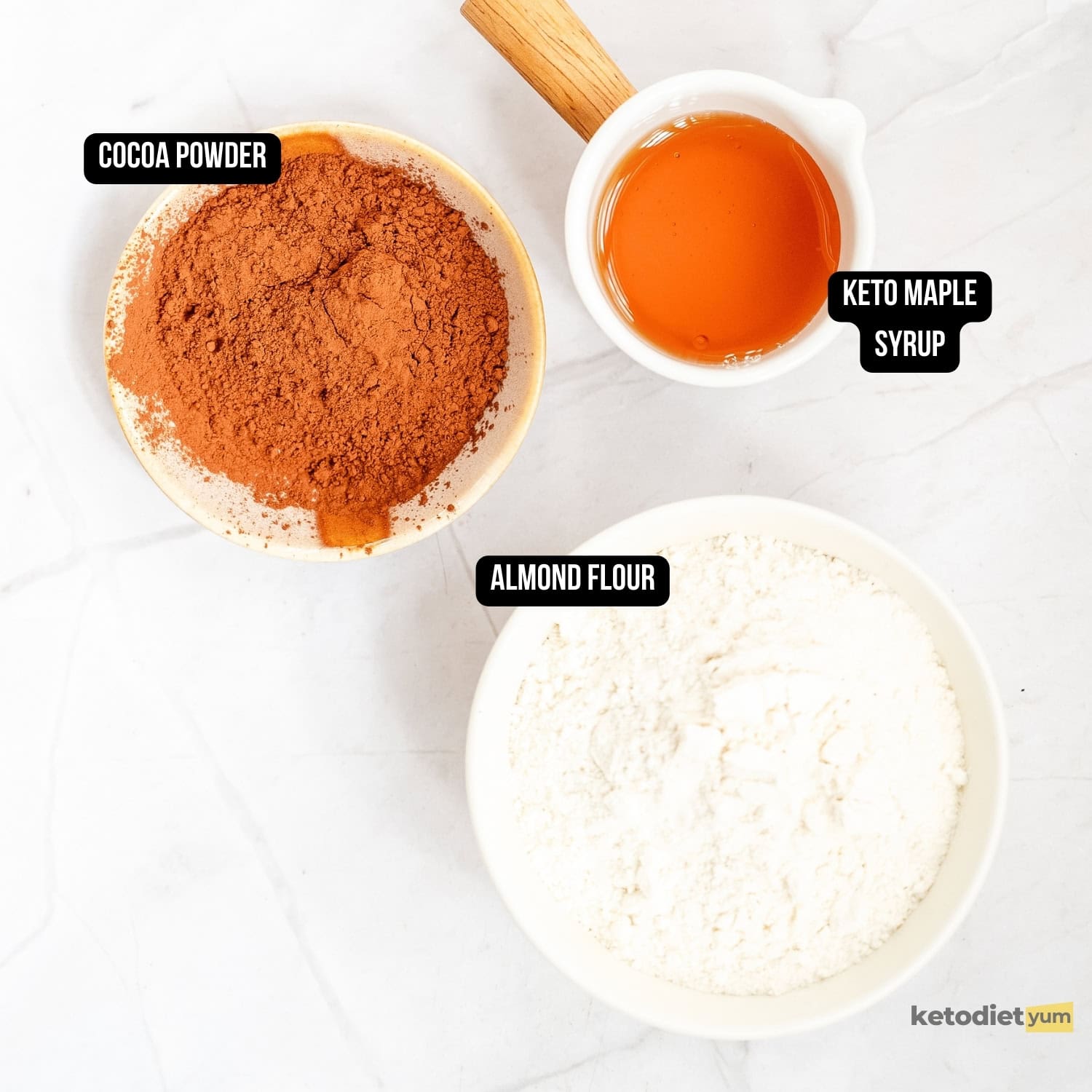 small bowls of ingredients filled with cocoa powder, almond flour, and keto maple syrup on a marble table