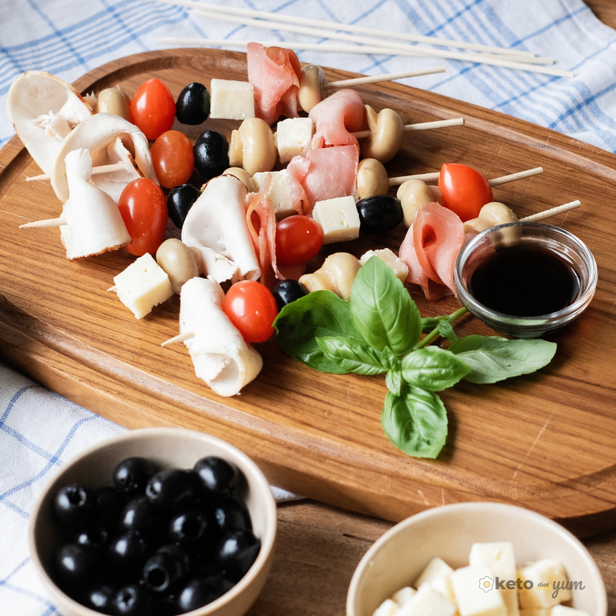 Easy Antipasto Skewers (Low Carb Appetizer) Colorful antipasto skewers arranged on a wooden platter with cherry tomatoes, cheese cubes, olives, deli meats, and marinated mushrooms, served with basil and balsamic glaze.