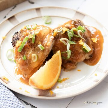 Orange Chicken Thighs (Better Than Takeout) Finished orange chicken thighs coated in citrus glaze, garnished with orange zest and green onions, served with an orange wedge.