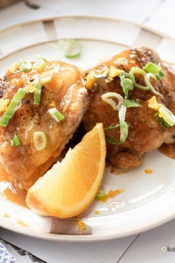 Orange Chicken Thighs (Better Than Takeout) Finished orange chicken thighs coated in citrus glaze, garnished with orange zest and green onions, served with an orange wedge.