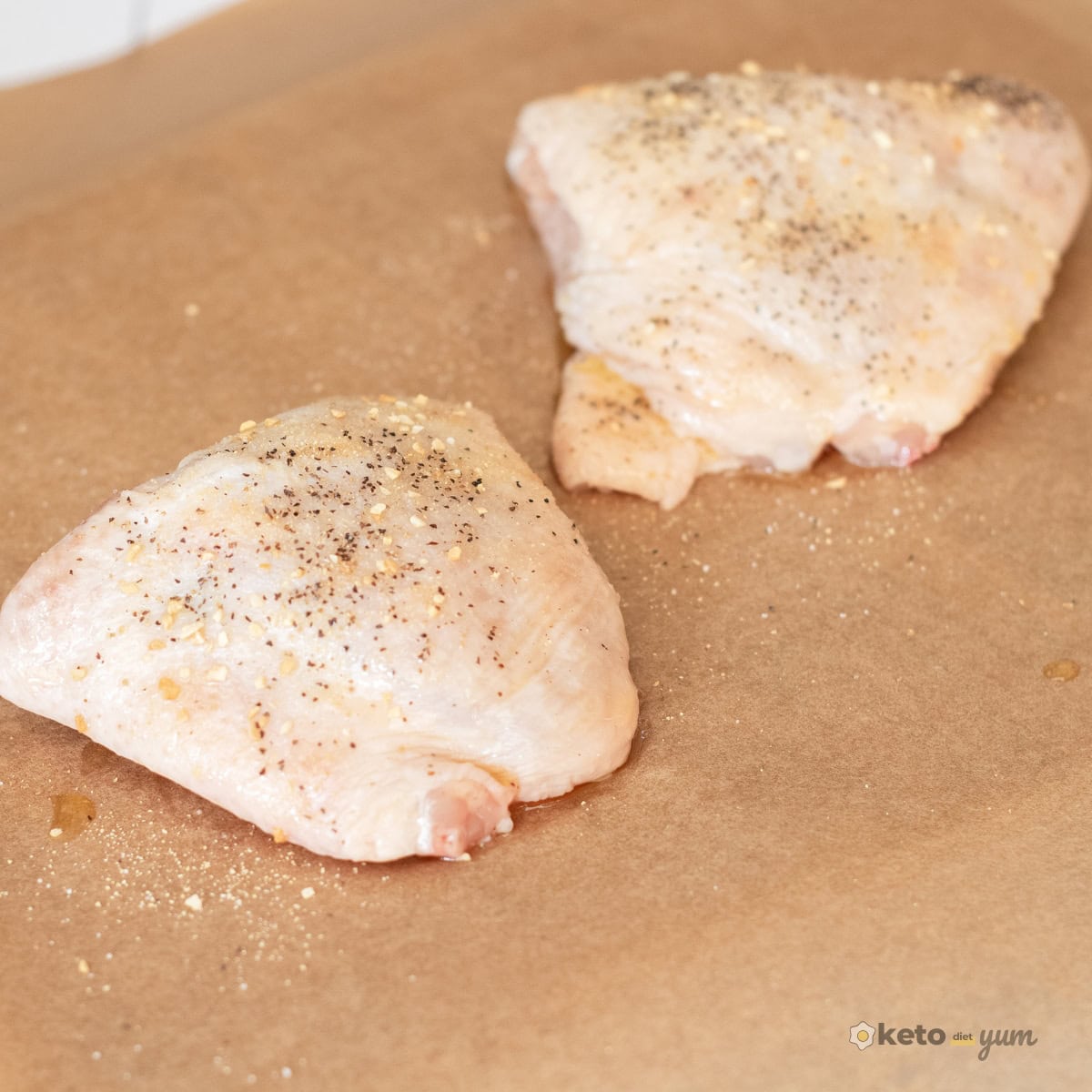 Orange Chicken Thighs (Better Than Takeout) Seasoned raw chicken thighs with salt, pepper, garlic, and onion powder on a parchment-lined baking tray before cooking.