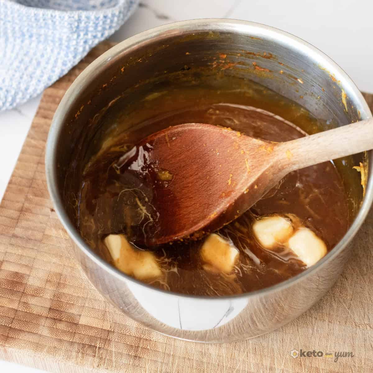 Orange Chicken Thighs (Better Than Takeout) Adding butter cubes to simmering orange sauce in a saucepan to create a rich and silky glaze for the chicken thighs.
