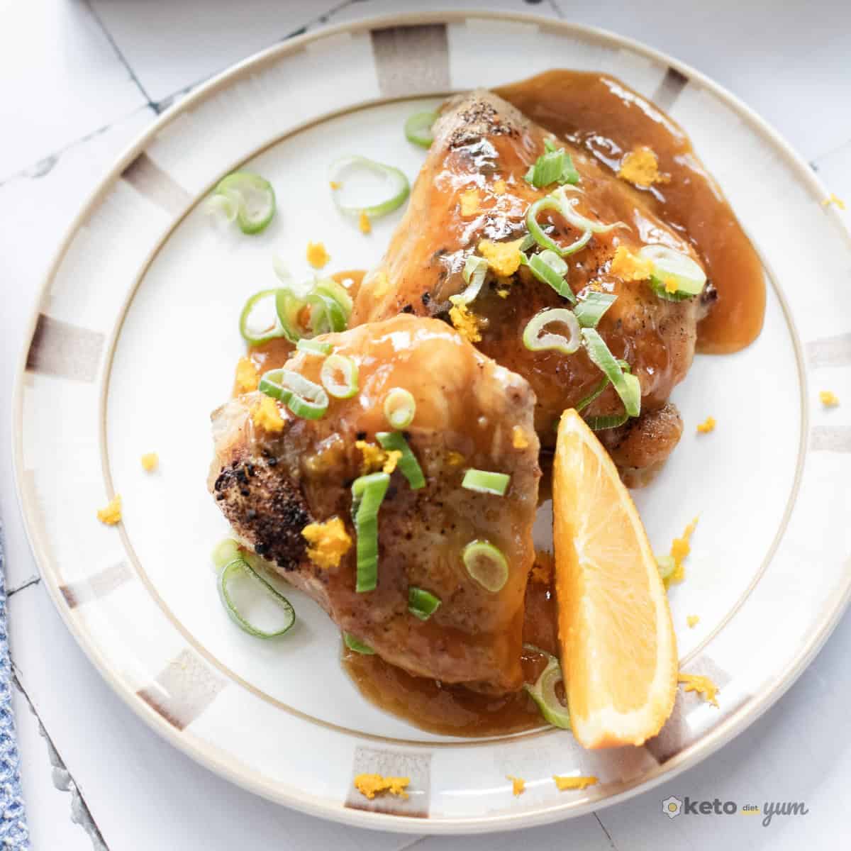 Orange Chicken Thighs (Better Than Takeout) Two baked orange chicken thighs with thick orange sauce, garnished with sliced green onions and fresh orange zest on a plate.
