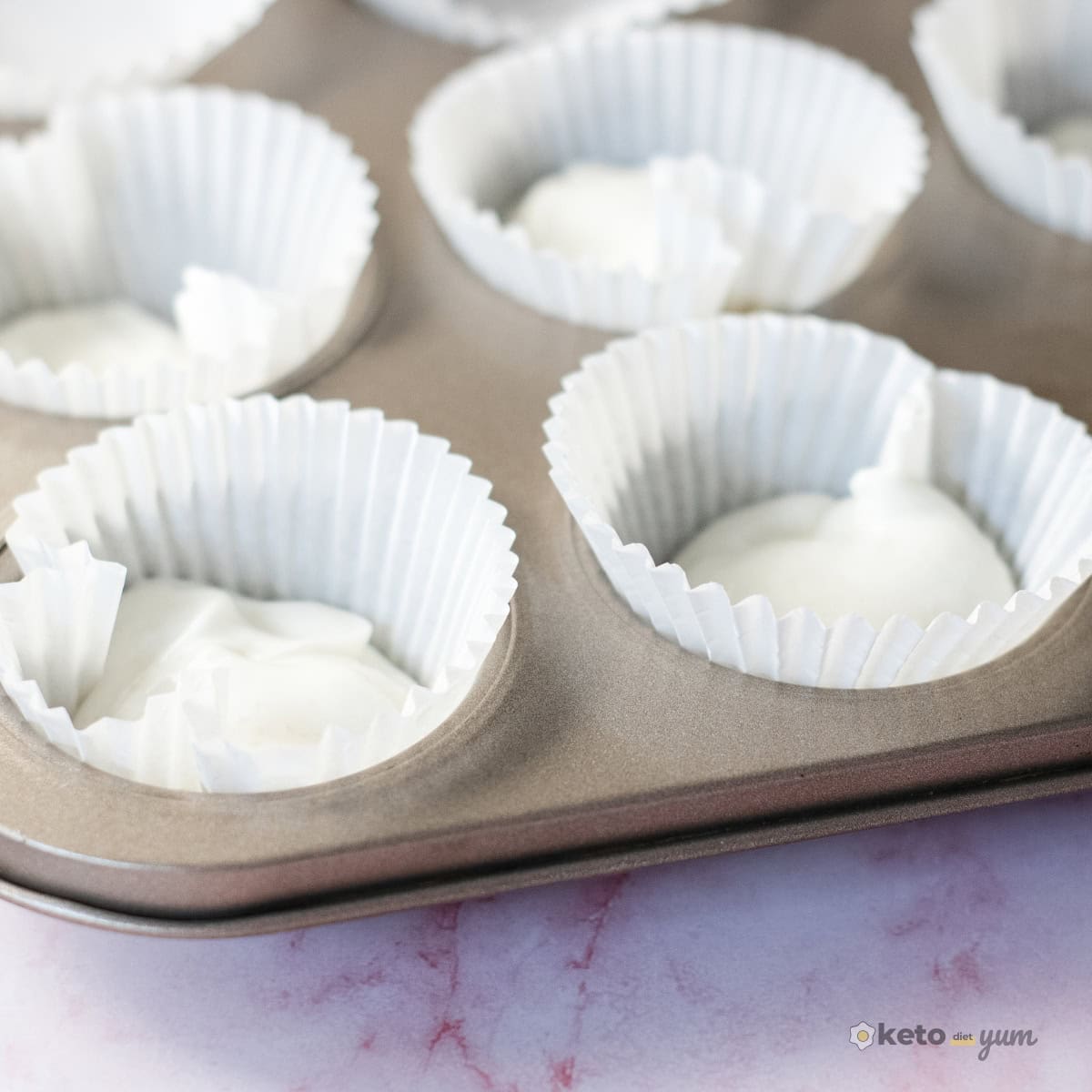 3 Ingredient Frozen Yogurt Bites Cupcake liners in a muffin tin filled with the first layer of sweetened Greek yogurt mixture for homemade frozen yogurt bites.
