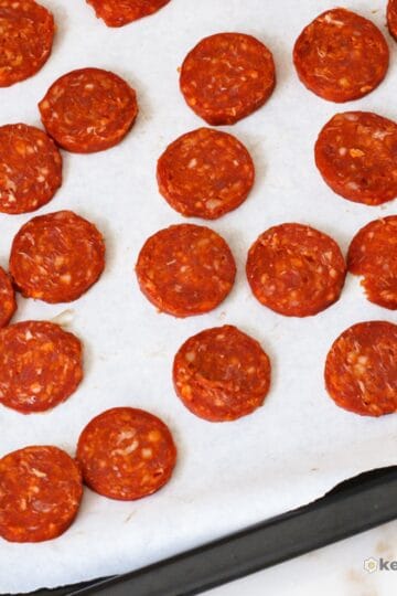 Sheet pan lined with baking paper topped with evenly spaced baked chorizo chips that are crispy and bright red. A simple high protein, zero carb keto snack option.