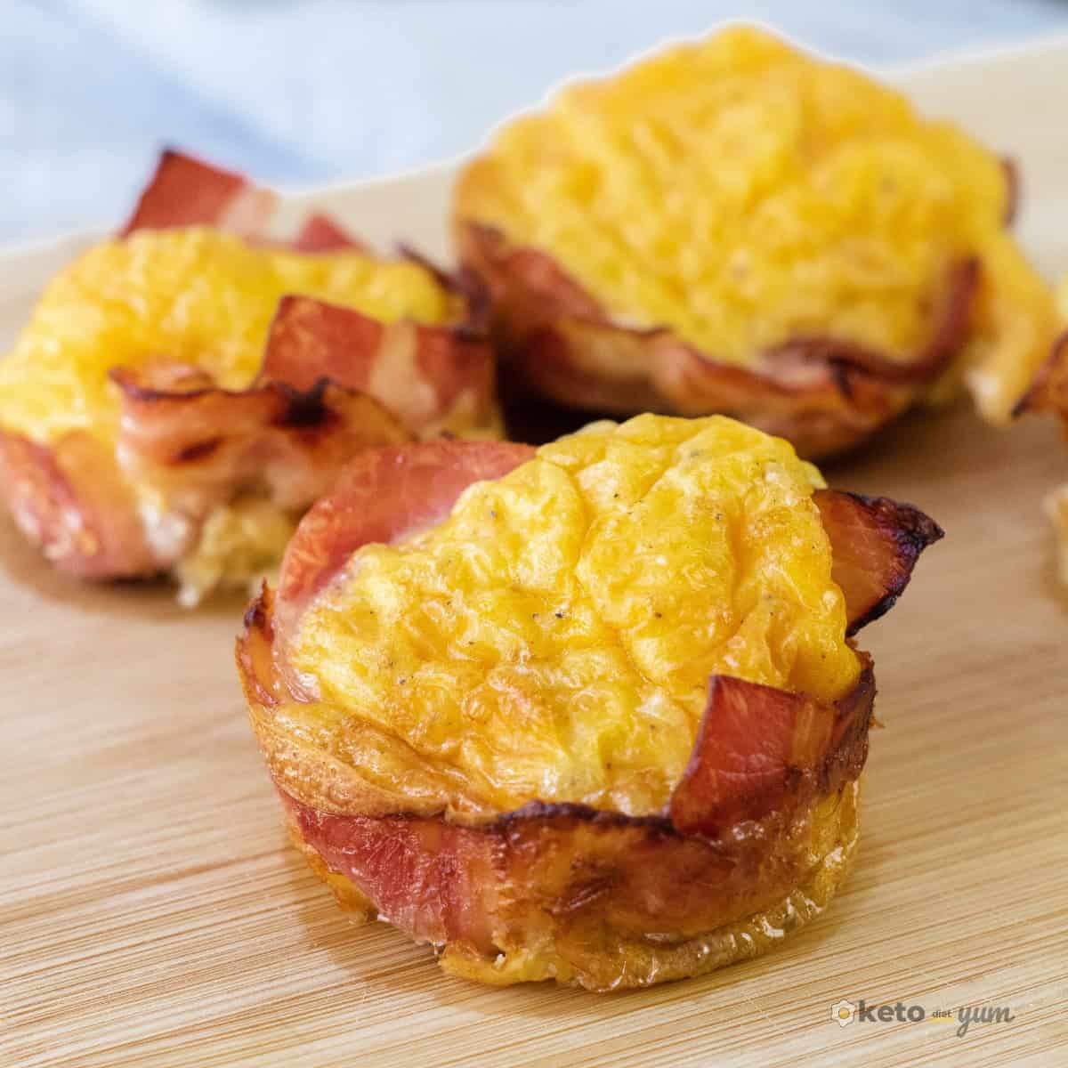 57 High Protein Snack Ideas for Busy Days and Craving Moments Close-up of baked bacon-wrapped egg muffin cups on a wooden board, showing their golden, fluffy centers and crispy bacon edges. A high protein, low carb keto snack perfect for meal prep.